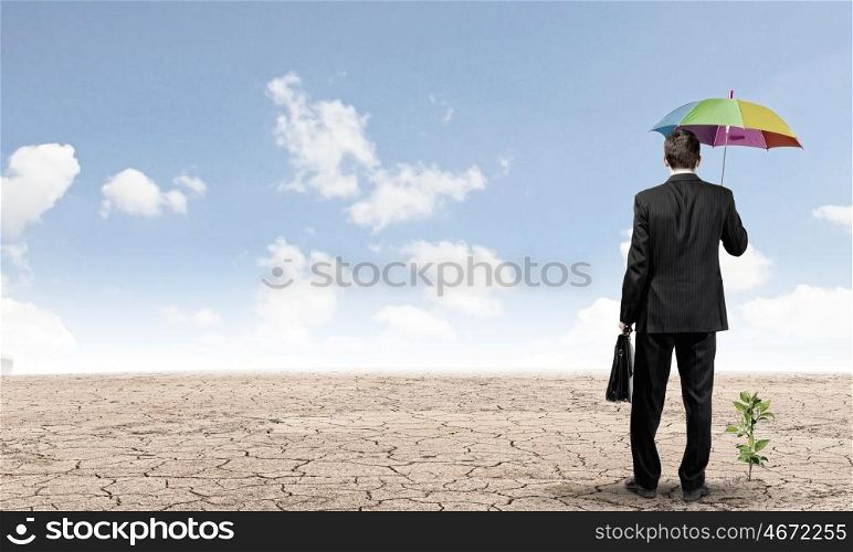 Money making. Rear view of businessman with umbrella protecting sprout