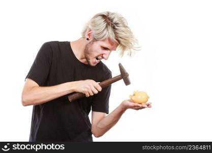 Money, savings, finances concept. Angry sreaming young blonde man wearing black t shirt trying to break piggy bank with hammer, studio shot isolated. Sreaming man trying break piggy bank with hammer