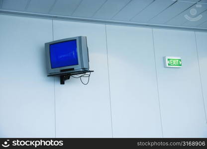 Monitor mounted to wall next to exit sign in airport