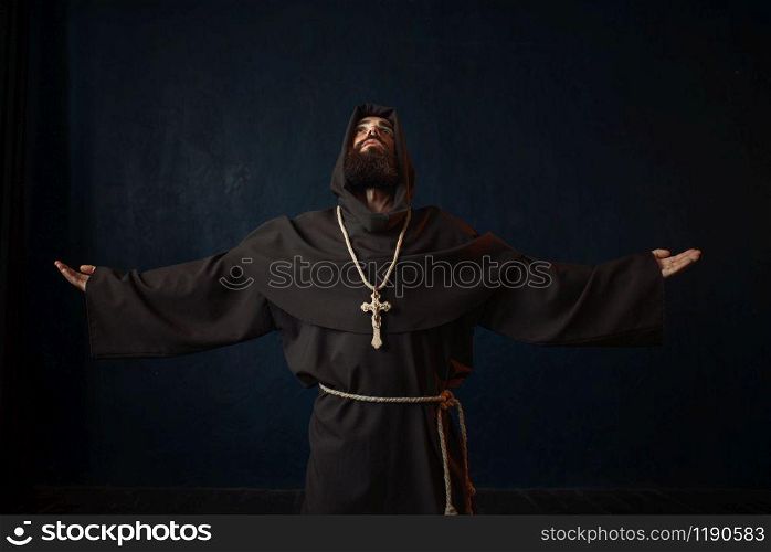 Monk in black robe with hood kneeling and praying, religion. Mysterious friar in dark cape. Monk in black robe with hood kneeling and praying