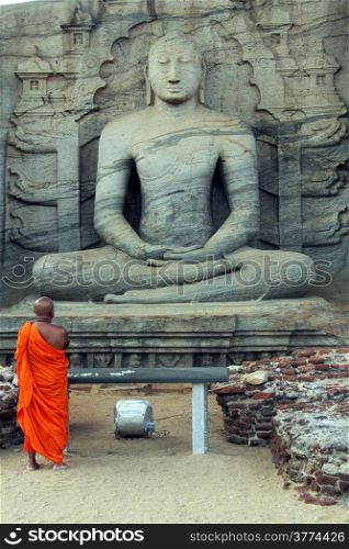 Monk pray near seated Buddha in Polonnaruwa, Sri Lanka