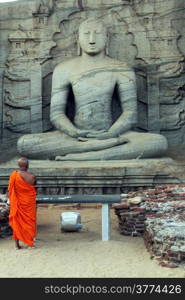 Monk pray near seated Buddha in Polonnaruwa, Sri Lanka