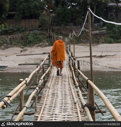 Monk walking on bamboo bridge over Nam Khan river, Luang Prabang, Laos