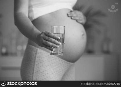 Monochrome closeup photo of expectant mother holding glass of water