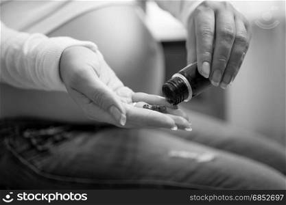 Monochrome closeup photo of pregnant woman holding pills on hand