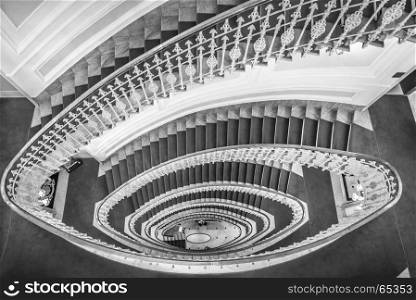 Monochrome image of spiral stairways made from marble with a red carpet and an elegant railing, view from above