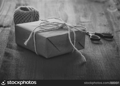 Monochrome image with a gift box wrapped in paper and tied with white string on a wooden table