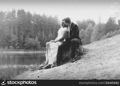 Monochrome photo of romantic just married couple hugging on log at riverbank