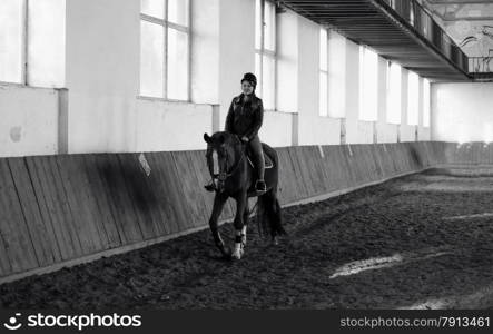 Monochrome photo of woman riding horse at indoor manege