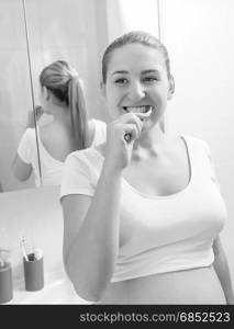 Monochrome portrait of young pregnant woman brushing teeth at bathroom