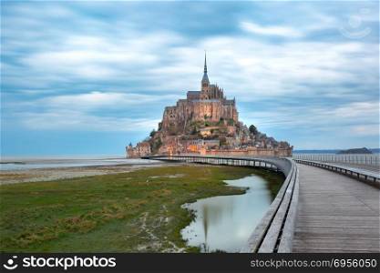 Mont Saint Michel at sunset, Normandy, France. Beautiful famous Mont Saint Michel with bridge and reflection in the canal at low tide in the cloudy morning, Normandy, France