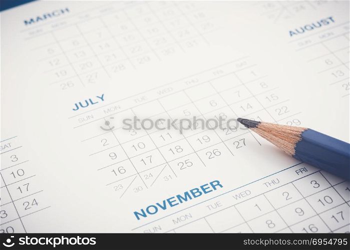 Months and dates of year and pencil on calendar sheet. Closeup shown dot prints, blurred at the edges, blue tone modern minimal style. Appointment schedule, timetable, business plan management.