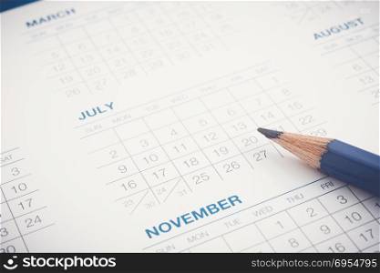 Months and dates of year and pencil on calendar sheet. Closeup shown dot prints, blurred at the edges, blue tone modern minimal style. Appointment schedule, timetable, business plan management.