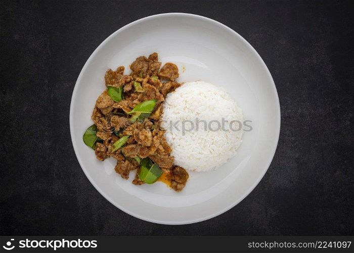 Moo Pad Prik Gaeng, Thai food, stir fried pork with red curry paste, bergamot leaves and yardlong beans with rice in ceramic plate on dark grey texture background