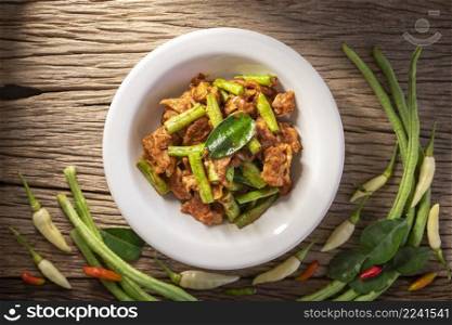 Moo Pad Prik Gaeng, Thai food, stir fried pork with red curry paste, bergamot leaves and yardlong beans on rustic natural wood texture background, top view