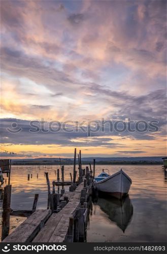 mood and tranquility at a lake coast with a boat at a wooden pier. Vertical view