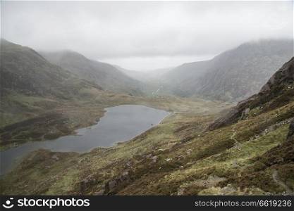 Moody landscape image of Llyn Idwal in Glyders mountain range in Snowdonia during heavy rainfall in Autumn