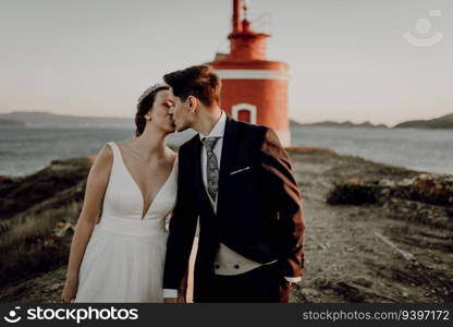 Moody portrait of a just married couple against a lighthouse at sunset