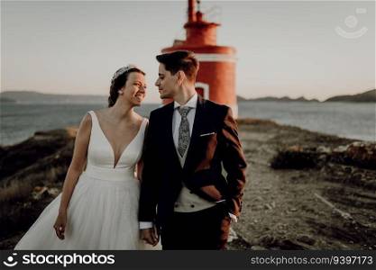 Moody portrait of a just married couple against a lighthouse at sunset