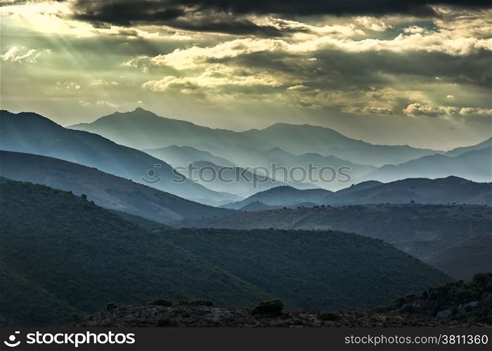 Moody skies and sunshine over receding mountains in the Balagne region of Corsica