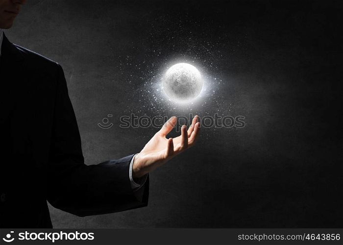 Moon glowing in darkness. Close up of businessman holding moon planet in palm
