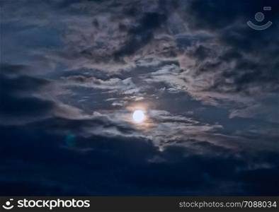 Moon in the night sky and moving clouds. long exposure shot. The moon looks through an opening in the clouds