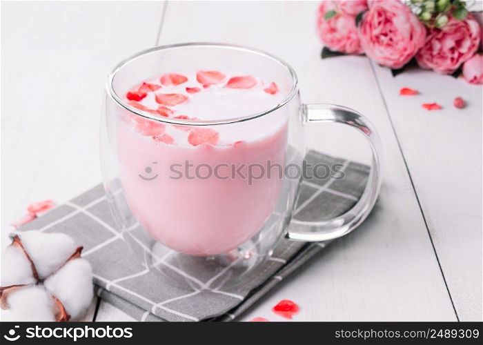 Moon milk. Pink matcha with rose petals. Transparent cup with trendy vegan whipped tea on a white background. Relaxing drink for sleepy time.. Moon milk. Pink matcha with rose petals. Transparent cup with trendy vegan whipped tea on white background. Relaxing drink for sleepy time.