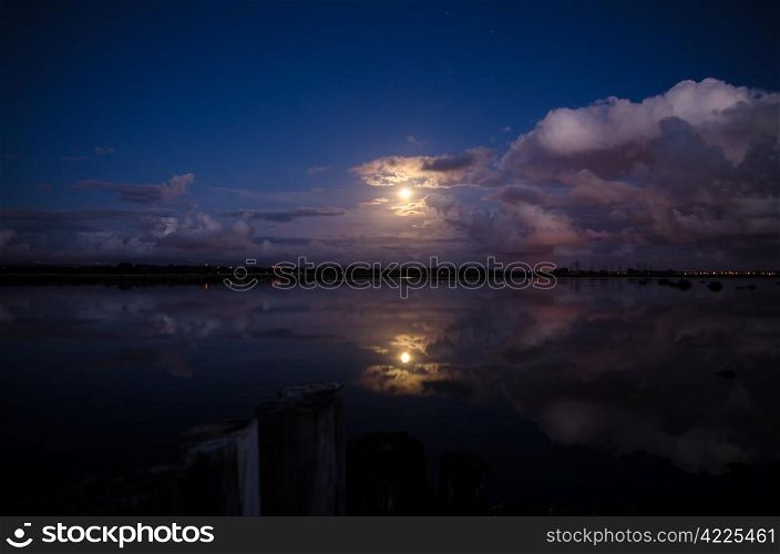 Moon rising and reflecting in the still water of a lake