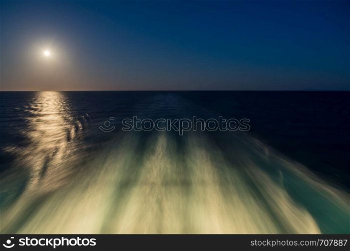 Moon rising over wake and waves of cruise ship at sea with concept of leaving or starting anew. Moon over the wake of cruise ship travelling at speed