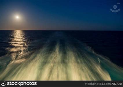 Moon rising over wake and waves of cruise ship at sea with concept of leaving or starting anew. Moon over the wake of cruise ship travelling at speed