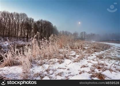 Moonlight in the winter dawn. Fog and mist on snowy winter river in Belarus.