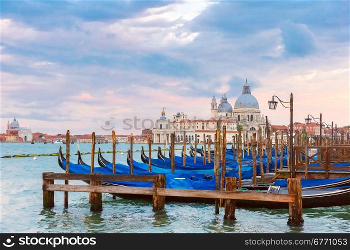 Mooring for gondolas on Piazza San Marco at sunset in Venice, Basilica of Saint Mary of Health or Basilica di Santa Maria della Salute on the background, Italy