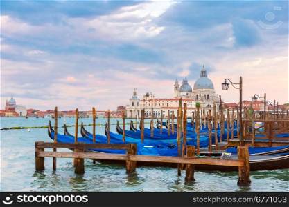 Mooring for gondolas on Piazza San Marco at sunset in Venice, Basilica of Saint Mary of Health or Basilica di Santa Maria della Salute on the background, Italy