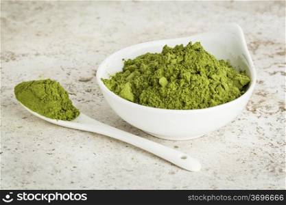 moringa leaf powder in a small bowl with a spoon against a ceramic tile background