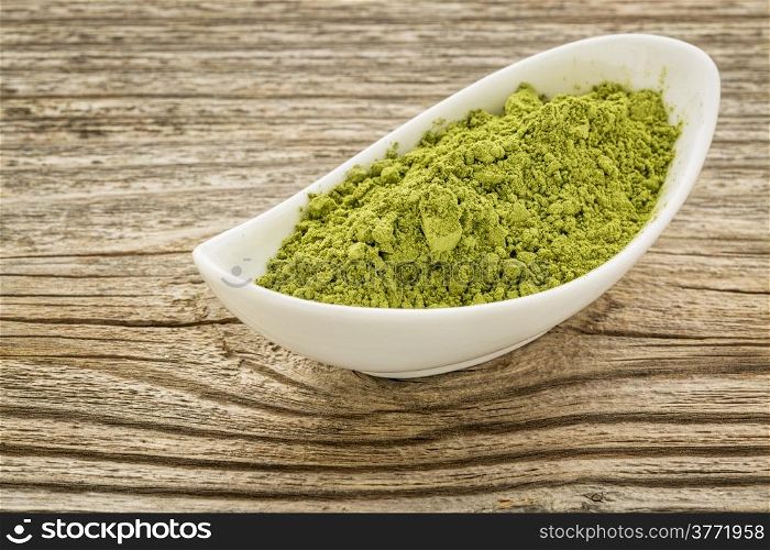 moringa leaf powder in a small ceramic bowl against grained wood