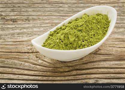 moringa leaf powder in a small ceramic bowl against grained wood