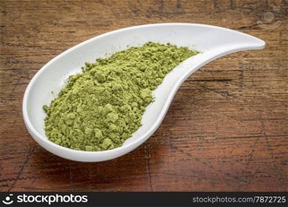 moringa leaf powder in a teardrop shaped bowl against rustic wood