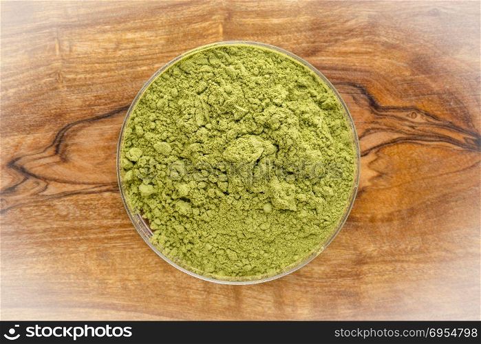 moringa leaf powder in around bowl agains olivetree wooden board