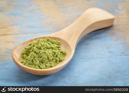 moringa leaf powder on wooden spoon against blue painted grunge wood