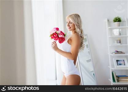 morning and people concept - beautiful young woman in white underwear with bunch of flowers at home window. woman in underwear with bunch of flowers at window