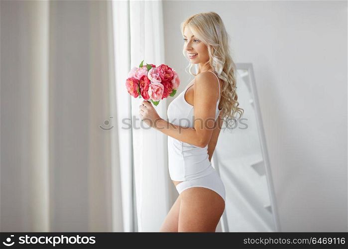 morning and people concept - beautiful young woman in white underwear with bunch of flowers at home window. woman in underwear with bunch of flowers at window
