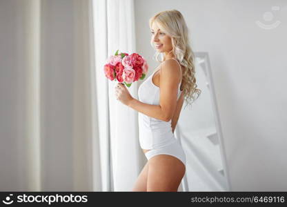 morning and people concept - beautiful young woman in white underwear with bunch of flowers at home window. woman in underwear with bunch of flowers at window