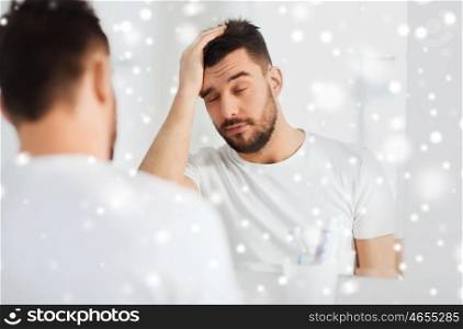 morning, awakening, hangover and people concept - sleepy young man in front of mirror at bathroom over snow