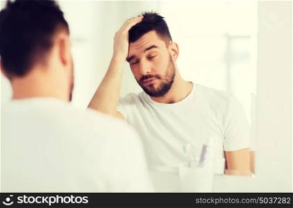 morning, awakening, hangover and people concept - sleepy young man in front of mirror at bathroom. sleepy young man in front of mirror at bathroom
