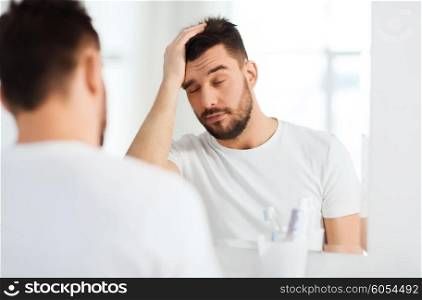 morning, awakening, hangover and people concept - sleepy young man in front of mirror at bathroom