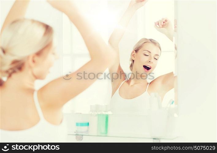 morning, awakening, morning and people concept - sleepy young woman yawning and stretching in front of mirror at bathroom. woman yawning in front of mirror at bathroom