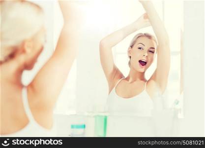 morning, awakening, morning and people concept - sleepy young woman yawning and stretching in front of mirror at bathroom. woman yawning in front of mirror at bathroom