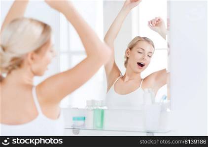 morning, awakening, morning and people concept - sleepy young woman yawning and stretching in front of mirror at bathroom