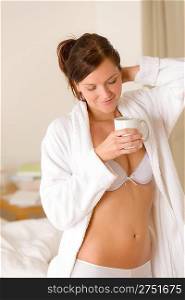 Morning bedroom - woman in bathrobe and lingerie with coffee waking up