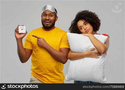 morning, bedtime and people concept - african american couple with alarm clock, eye sleeping mask and pillow over grey background. couple with alarm clock, sleeping mask and pillow